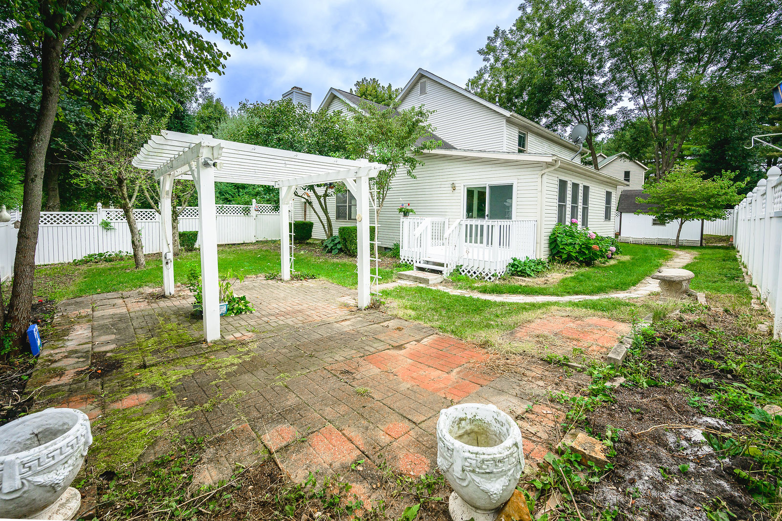 Wide view of the fenced backyard with pergola, patio, and hydrangeas